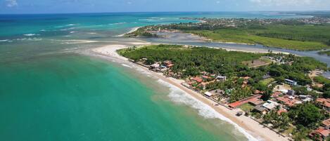 An aerial view of a coastal town with a beach, clear turquoise waters, and a mix of residential and commercial buildings.