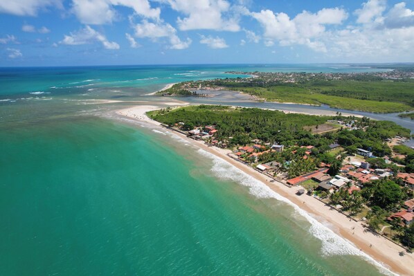 Vista aérea de un pueblo costero con playa, aguas turquesas cristalinas y una combinación de edificios residenciales y comerciales.