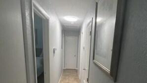 A narrow hallway with beige tiled flooring, white walls, and a door at the end. - River City Retreat (Sanford)