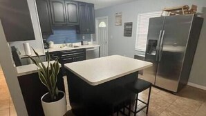 A kitchen with dark cabinets, a white countertop, a black bar stool, and a stainless steel refrigerator. - River City Retreat (Sanford)