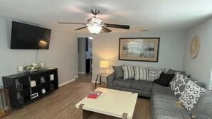 A living room with a sofa, a coffee table, a TV, and a ceiling fan. - River City Retreat (Sanford)