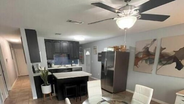 A modern kitchen with dark cabinets, a stainless steel refrigerator, and a dining area with a glass table and white chairs. - River City Retreat (Sanford)