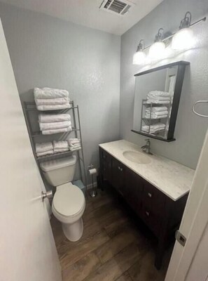 Casa de banho com sanita, lavatório, espelho e porta-toalhas.
