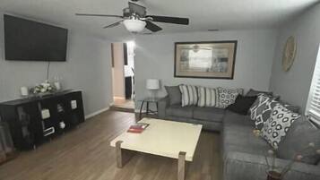 A living room with a sofa, a coffee table, a TV, and a ceiling fan.