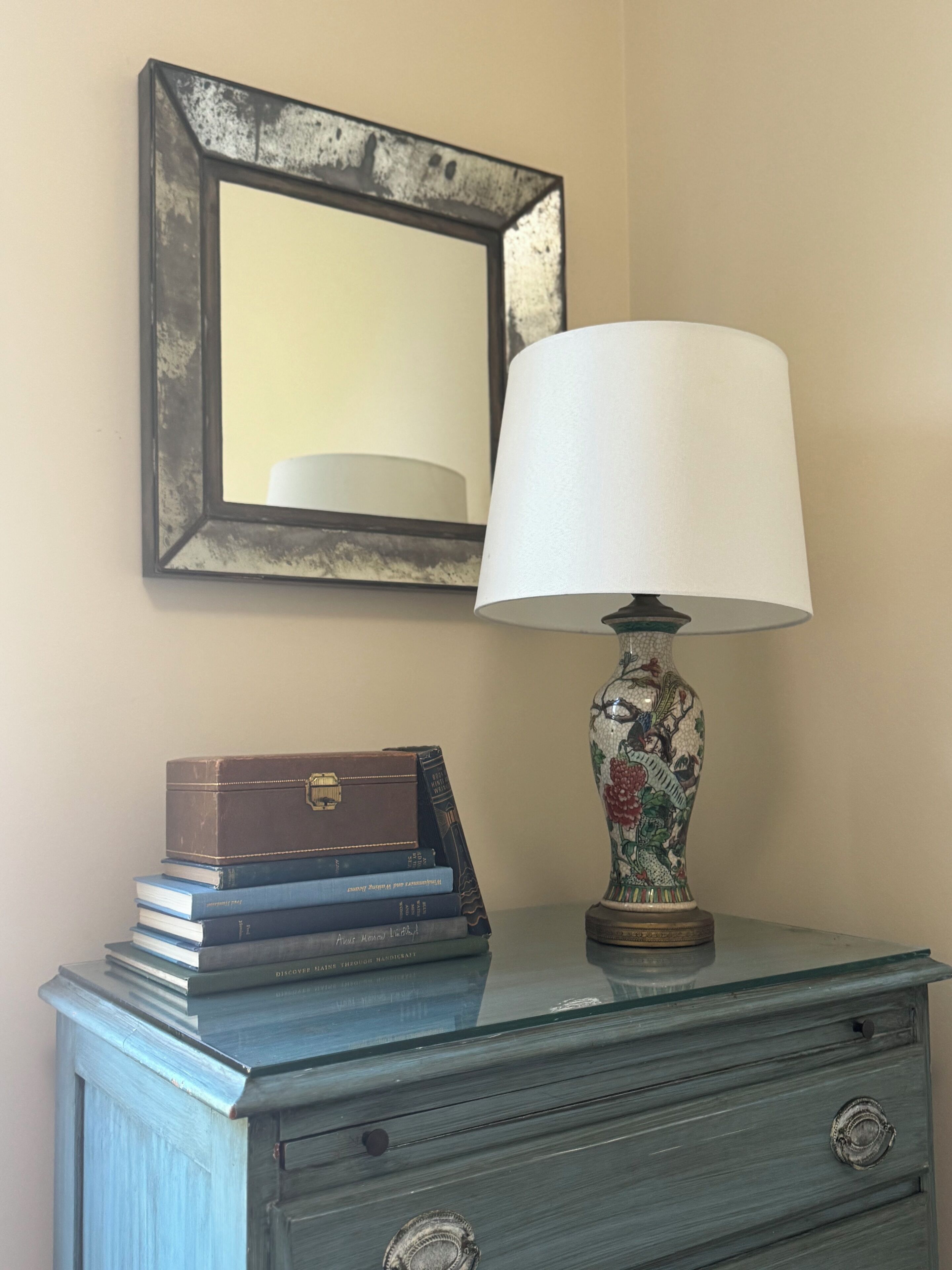 A dresser with a lamp, a mirror, and a stack of books.