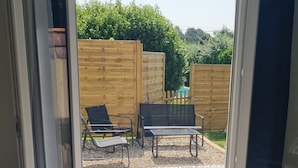 An open sliding door leading to a patio with a table, chairs, and a wooden fence in the background.