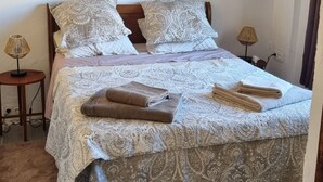A neatly made bed with patterned bedding, a painting of flowers on the wall, and a small table with a lamp beside it.