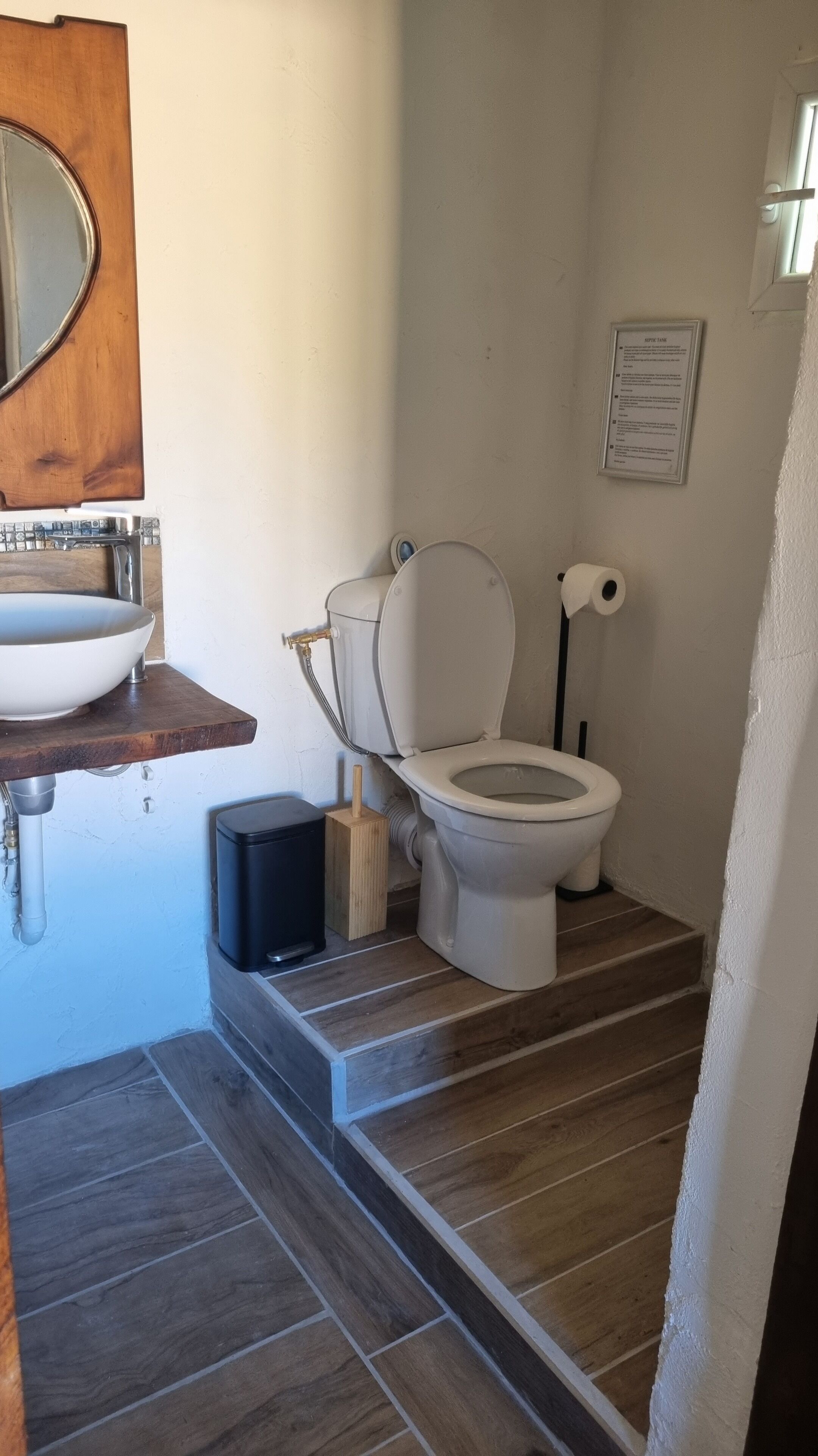 A bathroom with a wooden vanity, a white sink, a toilet, and a shower area.