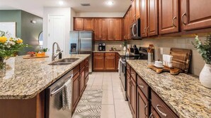 A modern kitchen with granite countertops, wooden cabinets, stainless steel appliances, and a central island. - Modern Luxury 5BR Pool Movie-Game Rm @Encore 7770 (Kissimmee)