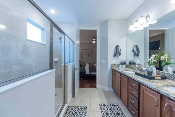 A modern bathroom with a glass shower enclosure, a large mirror, and a granite countertop.