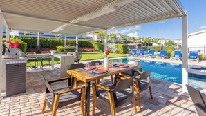 An outdoor pool area with a covered patio, lounge chairs, and a dining table set for four. - Modern Luxury 5BR Pool Movie-Game Rm @Encore 7770 (Kissimmee)
