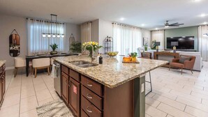 A modern kitchen with granite countertops, a central island, and a dining area with a chandelier. - Modern Luxury 5BR Pool Movie-Game Rm @Encore 7770 (Kissimmee)
