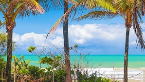 A view through a stone archway overlooking a beach with palm trees and a clear blue sky. - Pousada Ecoporto (Ipojuca)