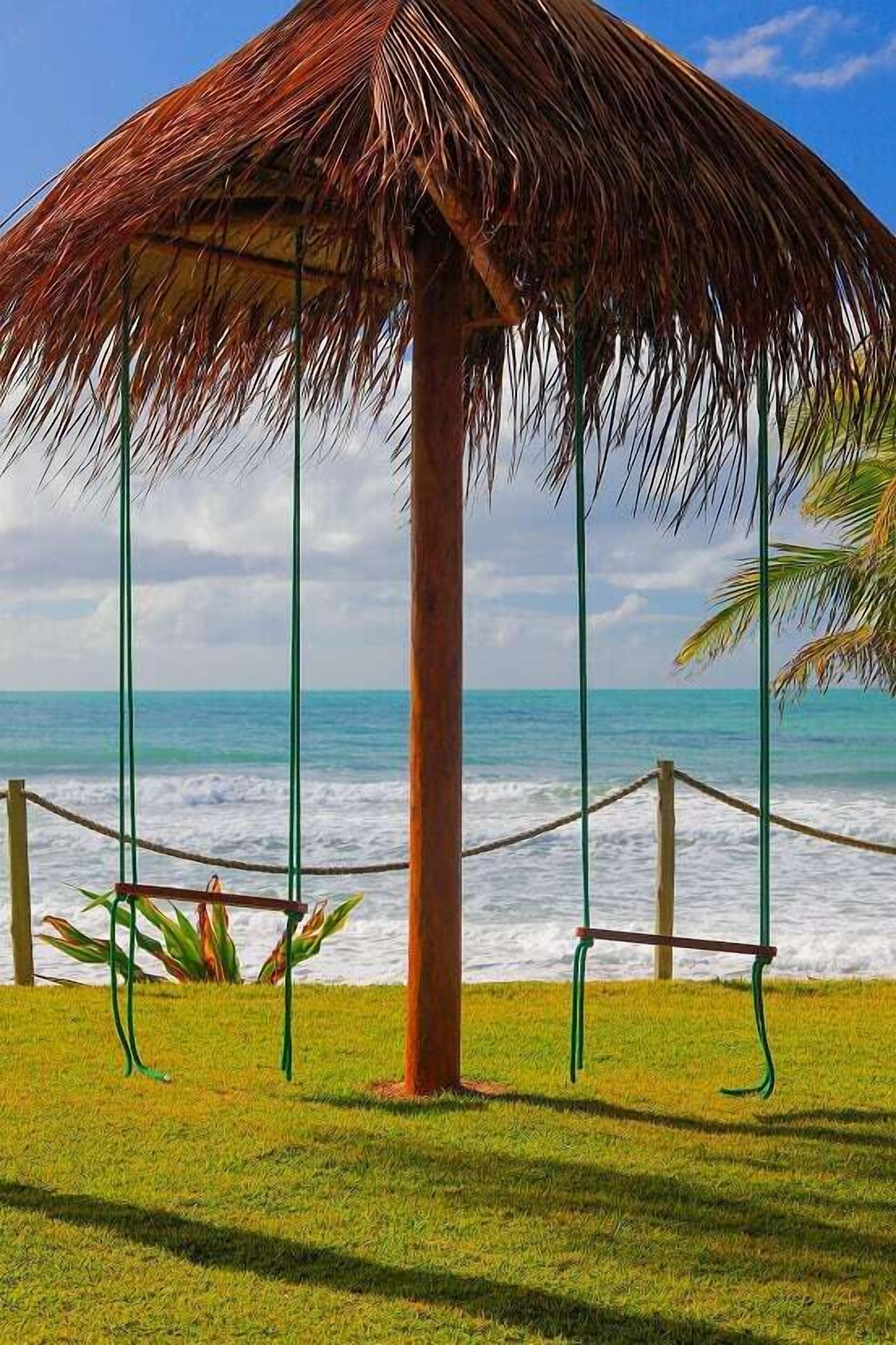 Estrutura com telhado de colmo e barreira de corda, com vista para uma praia e ondas.