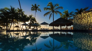 A pool area with palm trees, umbrellas, and lounge chairs. - Pousada Ecoporto (Ipojuca)