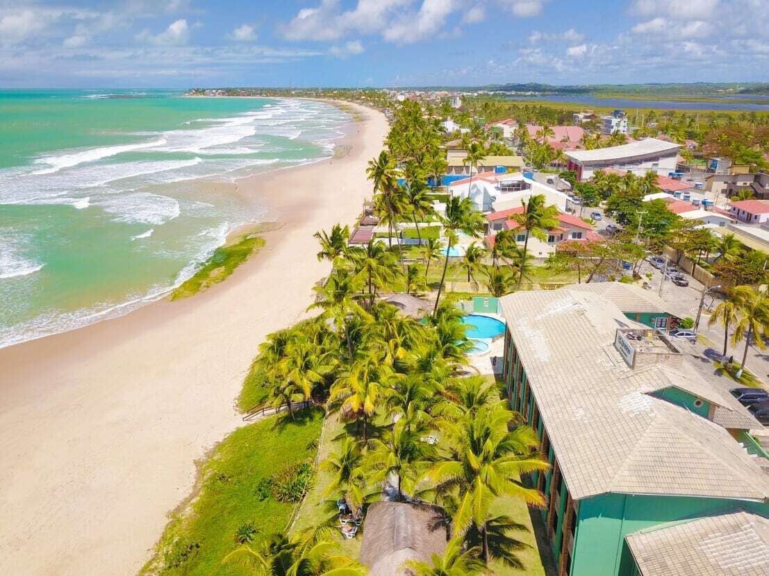 A coastal hotel with a beach view, palm trees, and a swimming pool.