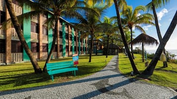 Un sendero que lleva a un edificio de fachada verde, con palmeras y vistas a la playa.