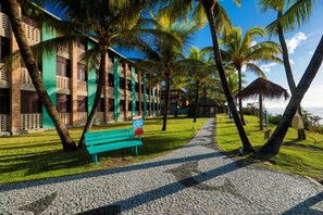 A pathway leading to a building with a green facade, palm trees, and a beach view. - Pousada Ecoporto (Ipojuca)