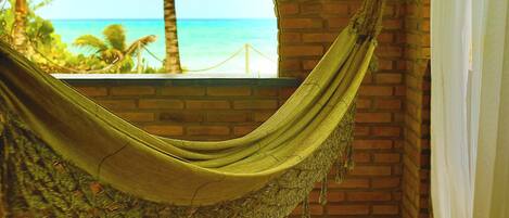 A hammock in a room with a brick wall and a view of the ocean.