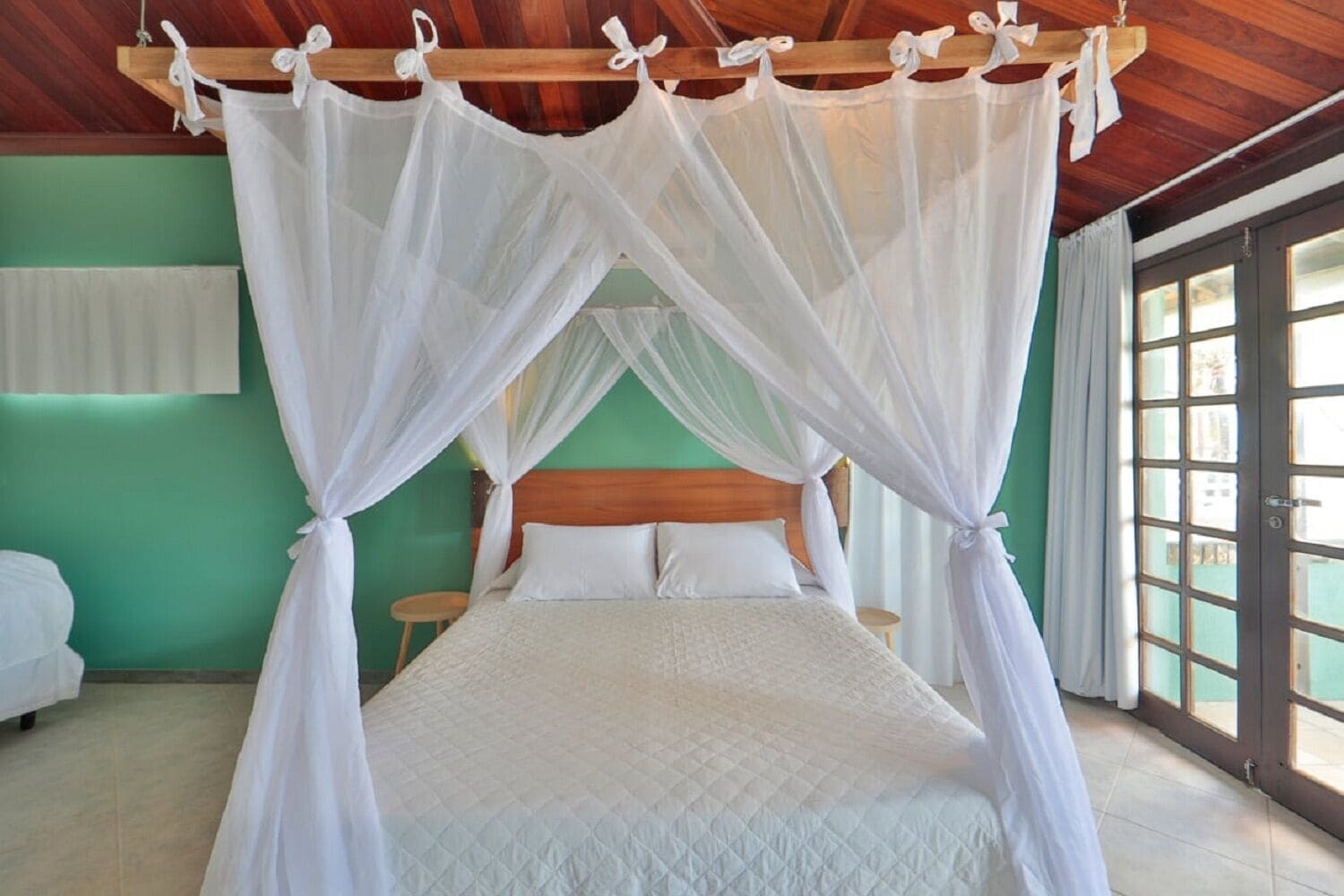 A bedroom with a bed under a canopy, a wooden headboard, a green wall, and a window with a view.