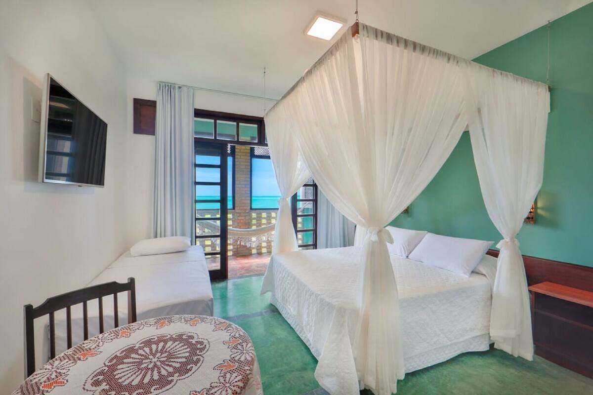 Habitación de hotel con cama, una silla, una mesa y vista al mar a través de un ventanal.