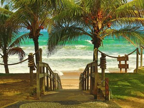 A wooden pathway leading to a beach with palm trees and a sign indicating a beachside location. - Pousada Ecoporto (Ipojuca)