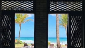 A hammock under a window with a view of the beach and palm trees. - Pousada Ecoporto (Ipojuca)