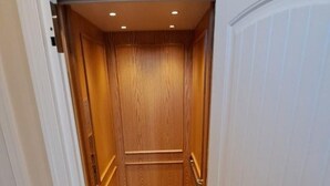 Un pasillo estrecho que conduce a un ascensor, con paredes de madera y suelo de baldosas.