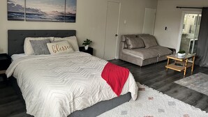 A bedroom with a bed, a sofa, a small table, a mirror, and artwork on the wall.