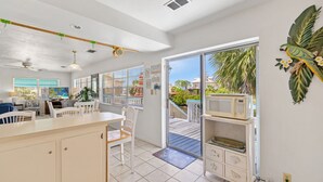 A bright kitchen with a large island, white cabinetry, and a view of a wooden deck and palm trees.
