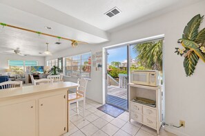 A bright kitchen with a large island, white cabinetry, and a view of a wooden deck and palm trees.