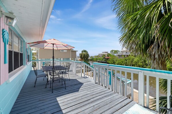 A wooden deck with a table and chairs, a striped umbrella, and a view of the water and buildings in the background.