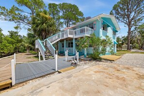 A two-story house with a wooden deck and a staircase leading to the upper floor.