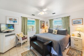 A bedroom with a bed, a desk, a chair, a nightstand, and a ceiling fan.