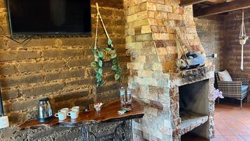 Un interior rústico con pared de ladrillo, un televisor de pantalla plana montado sobre una mesa de madera con tazas y una tetera, y una chimenea de piedra.