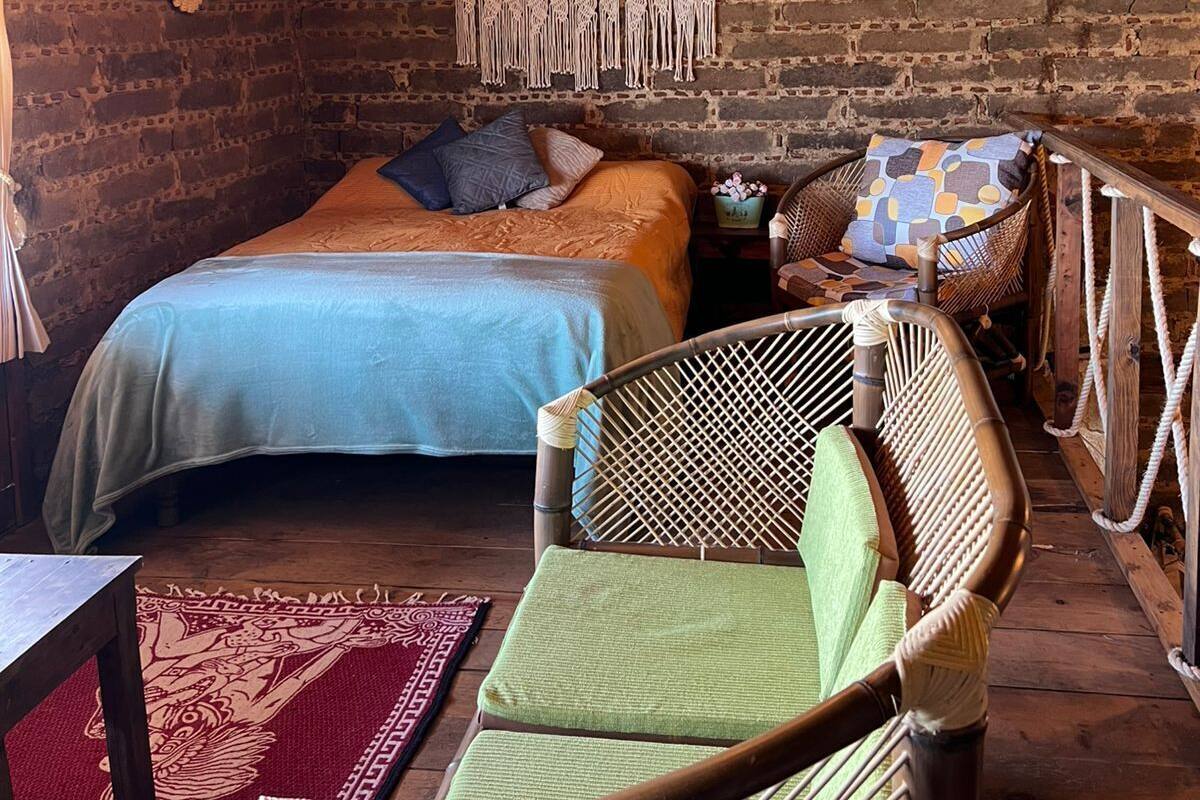 A rustic room with a bed, a chair, a macramé wall hanging, and a wooden ceiling.