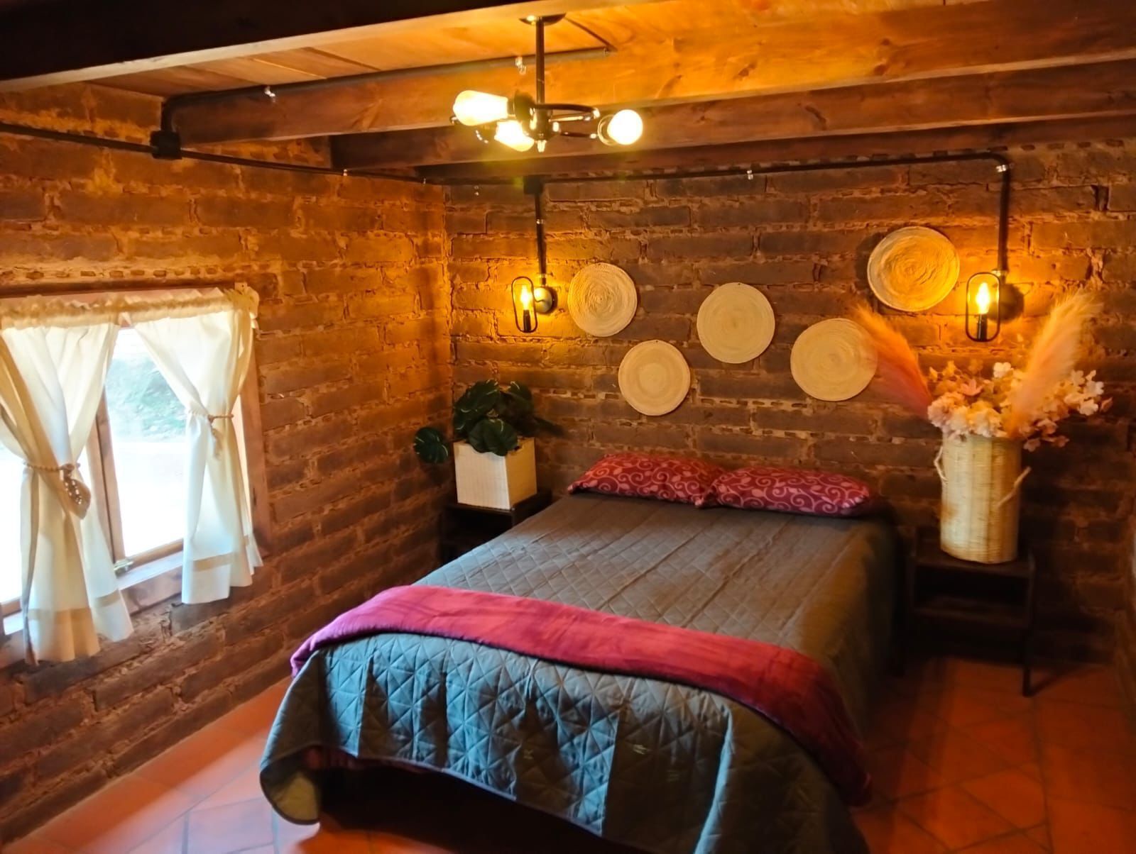 A cozy room with a bed, a window with curtains, a wall-mounted light fixture, and a decorative wall with circular items.
