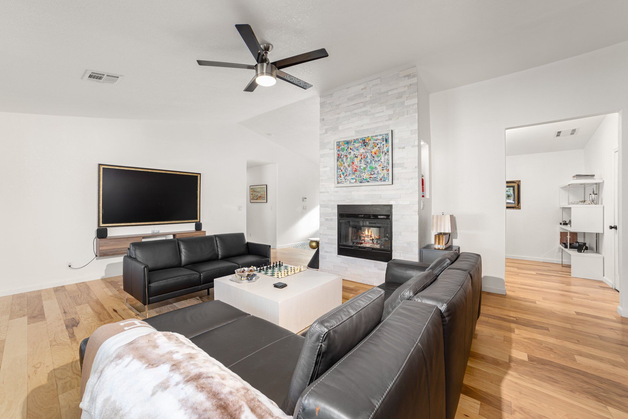 A modern living room with a fireplace, a flat-screen TV, and a ceiling fan.