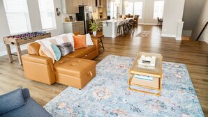 A spacious living room with a sofa, ottoman, and coffee table, a kitchen in the background, and a dining area with chairs. - Brand New! Huge 3-bedroom, 2,500 sqft  3rd and 4th floor condo, private rooftop. (Raleigh)
