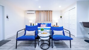Une chambre moderne avec un lit, deux chaises bleues, une petite table avec une plante et des bouteilles, et une armoire blanche.