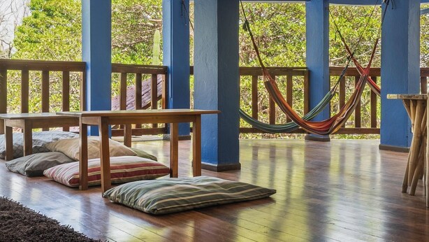 Un espacio al aire libre techado con suelo de madera, bancos y una hamaca.