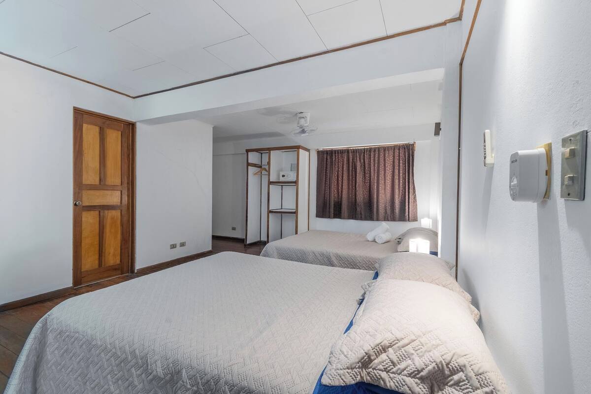 A hotel room with two beds, a wardrobe, a desk, and a bathroom visible through an open door.