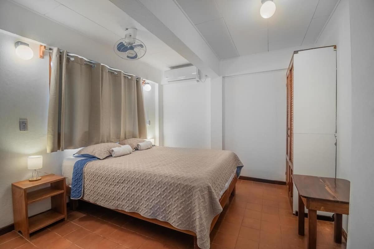 A bedroom with a bed, a nightstand, a wooden table, and a ceiling fan.