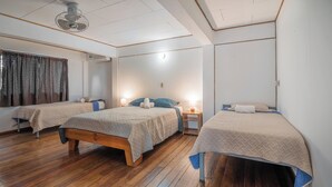 Una habitación de hotel con dos camas, piso de madera, ventilador de techo y una ventana con cortinas.