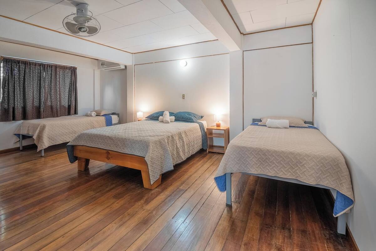 A hotel room with two beds, wooden flooring, a ceiling fan, and a window with curtains.