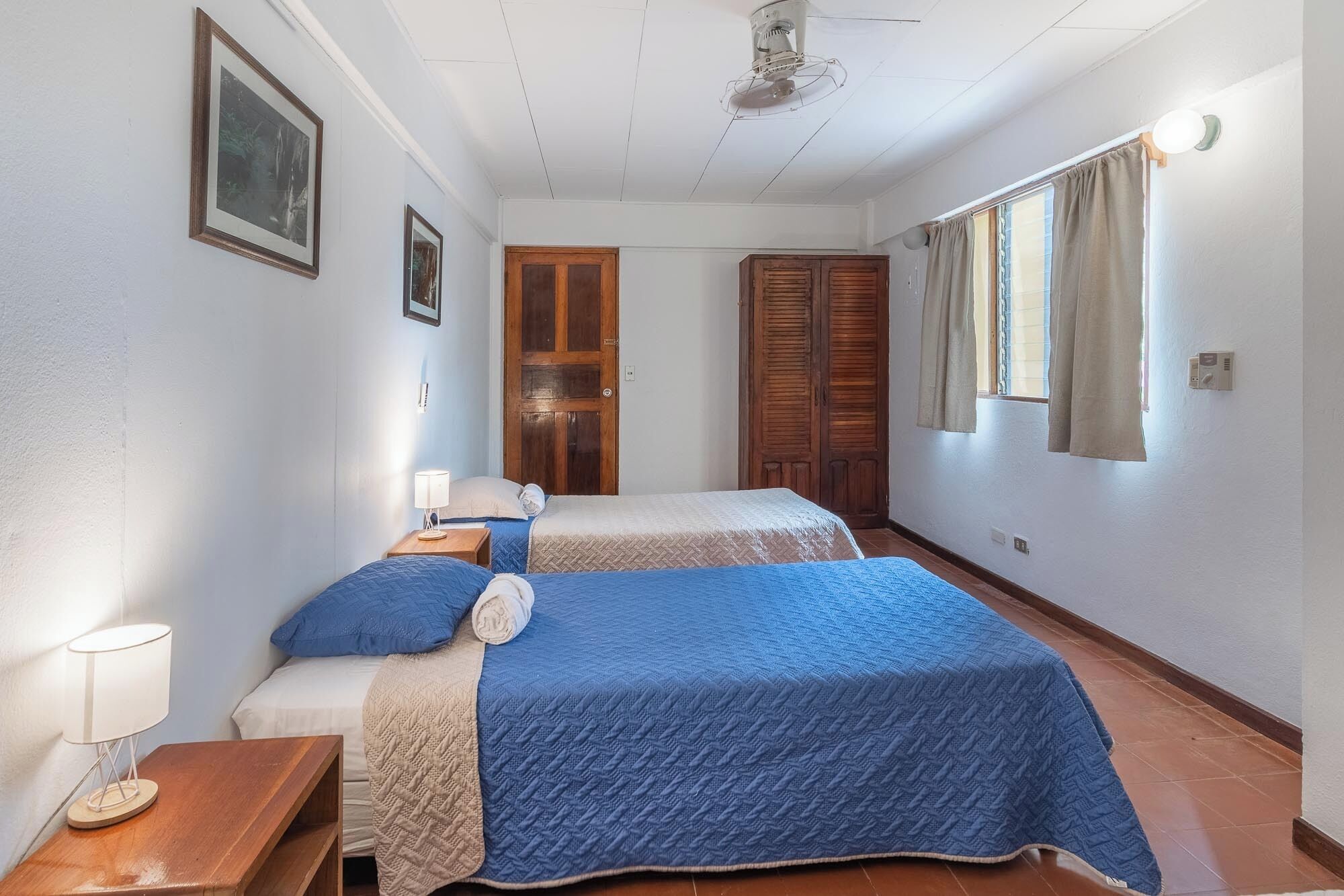 A bedroom with two beds, wooden wardrobe, and a window with curtains.
