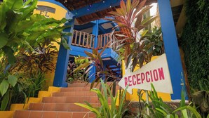 Entrada de un edificio con un cartel que dice 'RECEPTION' y una escalera que sube a un edificio azul y amarillo.