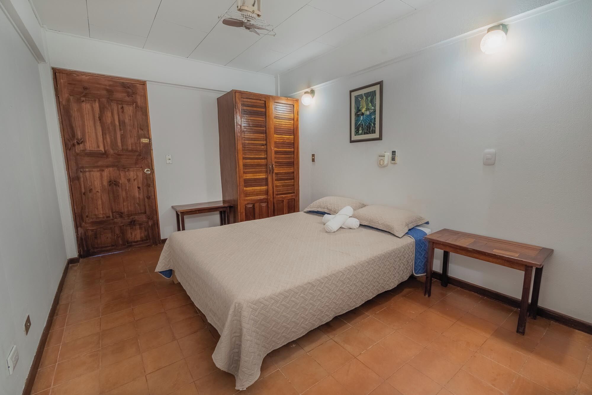 A bedroom with a bed, wooden wardrobe, and a painting on the wall.