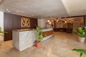 A reception area with a wooden panel wall, a marble reception desk, and potted plants. - Lux 2BR Penthouse w/Private Plunge Pool/Aldea Zama (Tulum)