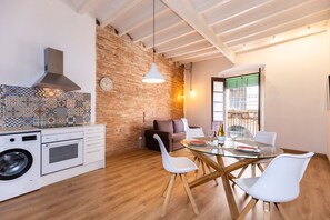 A modern kitchen with a washing machine, a dining area with a glass table and white chairs, a brick wall, and a hanging light fixture. - Merceria 3 by Unik Tarragona (Tarragona)